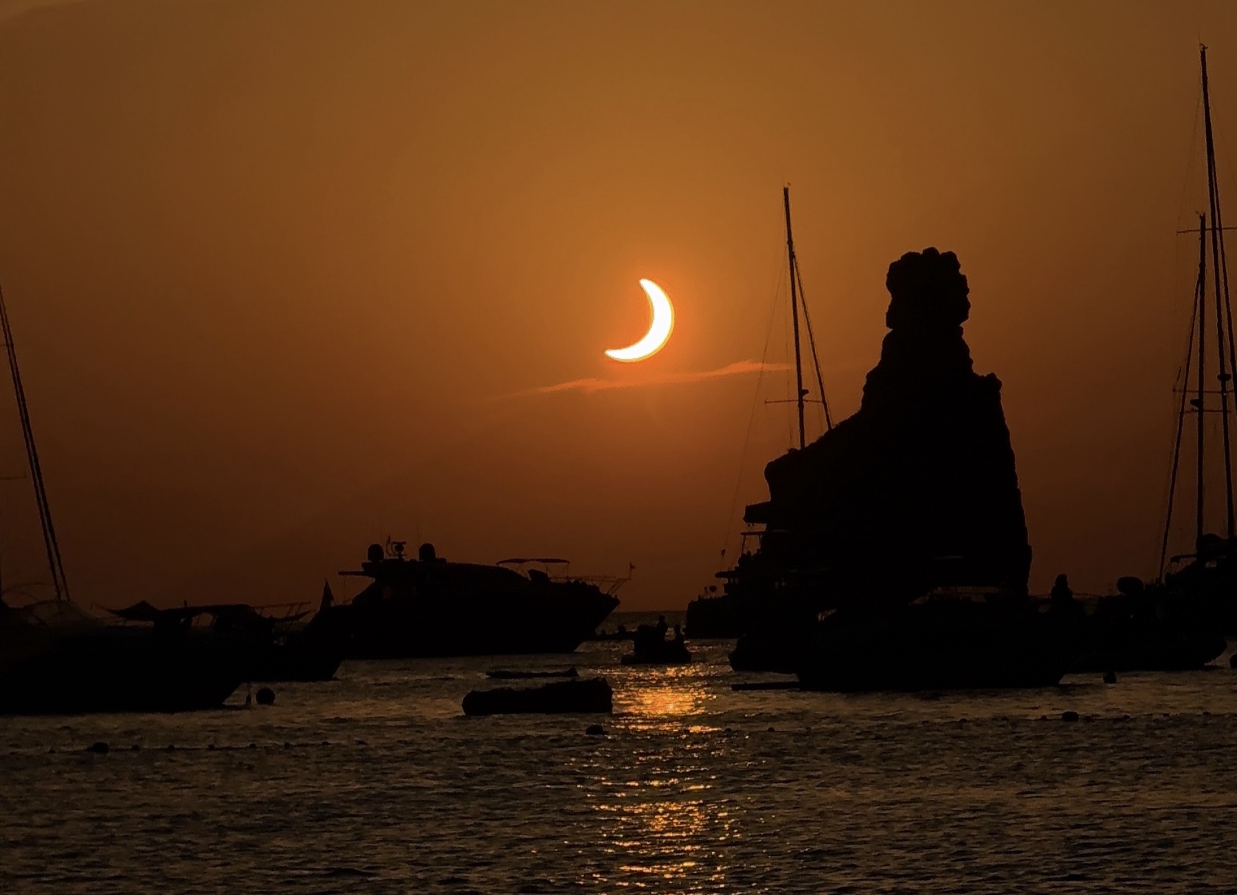 Le soleil en croissant au-dessus de la mer, silhouettes du rocher et des bateaux.